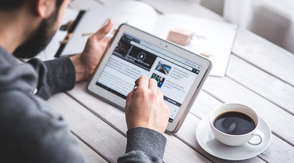 A man reading a website on a tablet while drinking coffee in a café